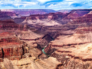 Grand Canyon river winding through a deep chasm with layered rock formations under a partly cloudy textured sky.