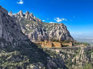 Montserrat Monastery nestled beneath towering rocky pinnacles and rugged mountain cliffs under a brilliant blue sky in Catalonia, Spain