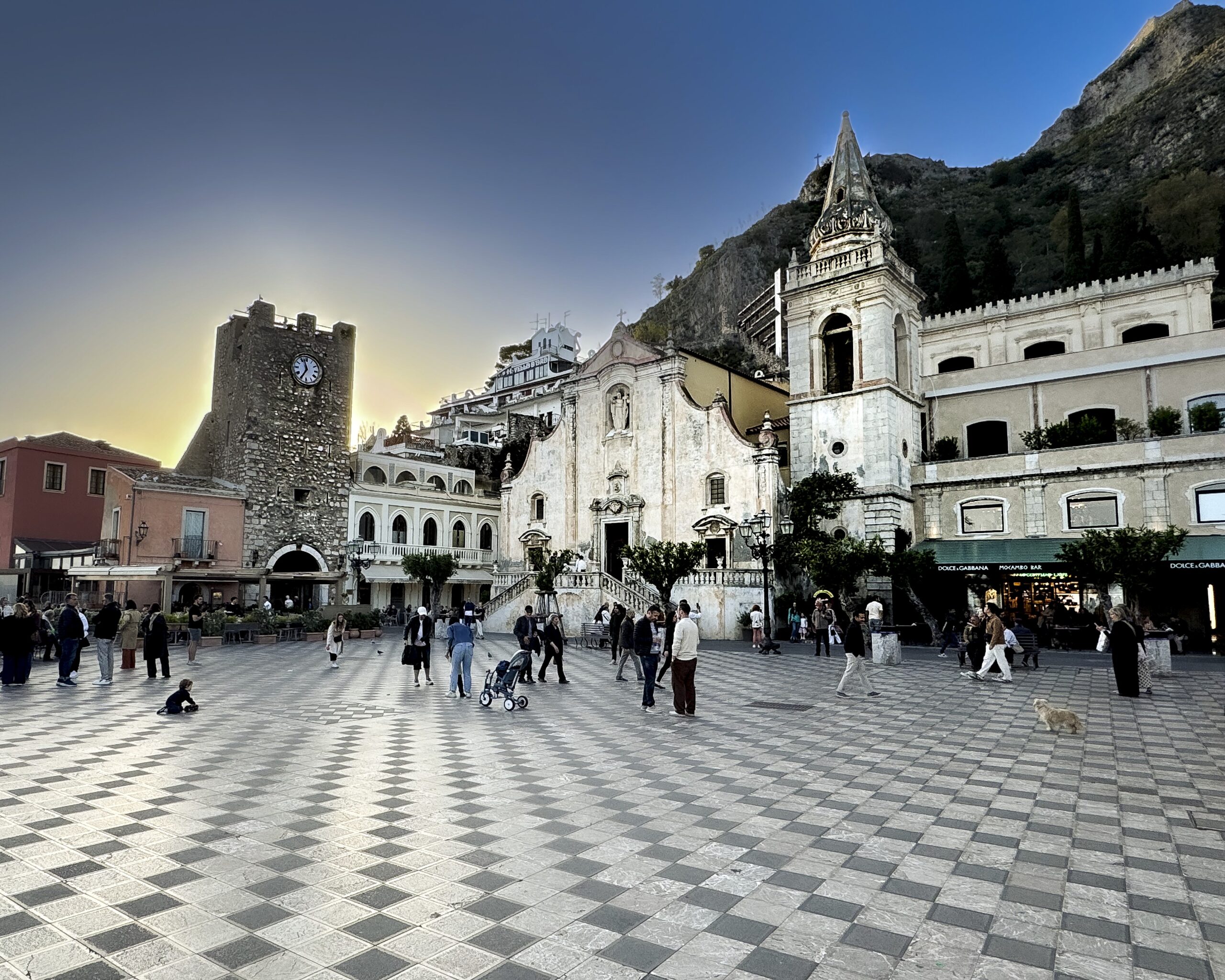 Twilight sky behind the historic clock tower and St. Joseph Church in Piazza IX Aprile, Taormina, with iconic checkered tile square.